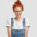 Horizontal shot of pleasant looking ginger young European woman in round transparent glasses, stylish dungarees, poses against white background, has glad expression. People and emotions concept.